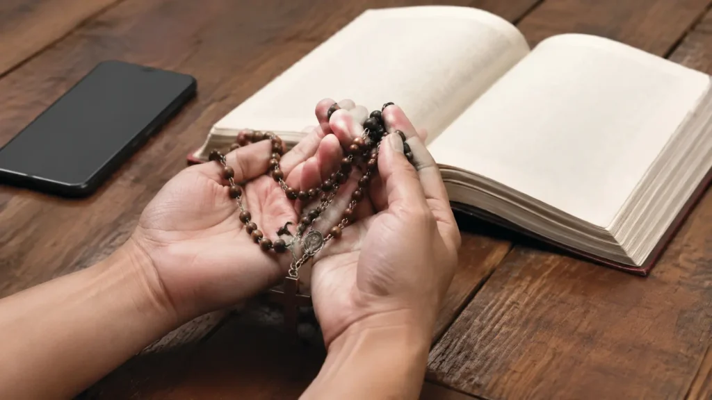 Mãos com rosário diante de uma Bíblia e celular sem notificações.